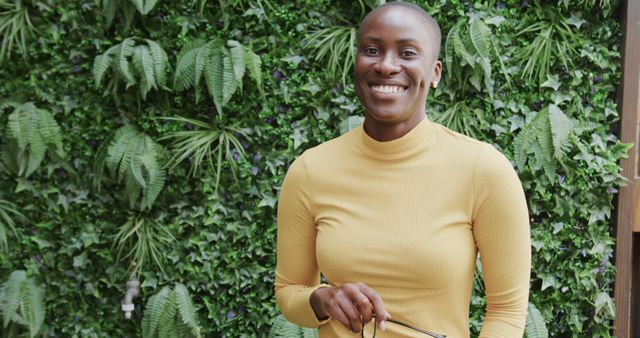 Smiling Woman in Yellow Sweater Holding Personal Accessories, Green leafy Wall - Download Free Stock Images Pikwizard.com