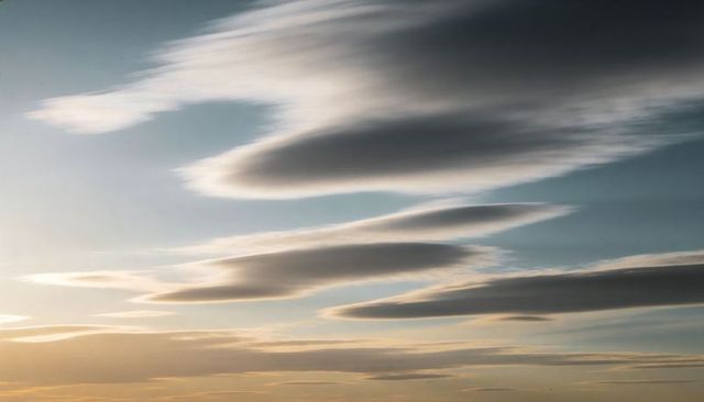 Stacked lenticular clouds forming layered discs over pastel sunset horizon