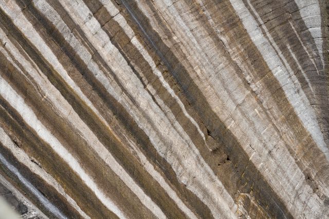 Detailed shot of a sedimentary rock formation showing distinct layers and striations, perfect for educational materials on geology and earth science. Could be used in geological surveys, textbooks, or as background texture in design projects emphasizing natural patterns or earth tones.