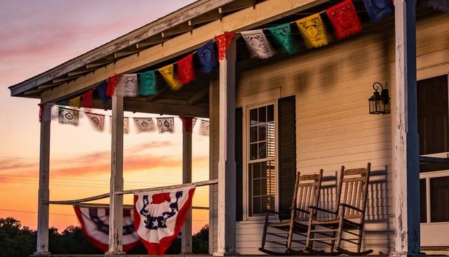 Rocking chairs casting sunset shadows on weathered porch with patriotic bunting at twilight