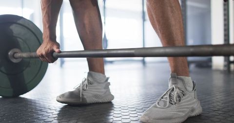 Man lifting barbell in gym with athletic shoes and smartwatch