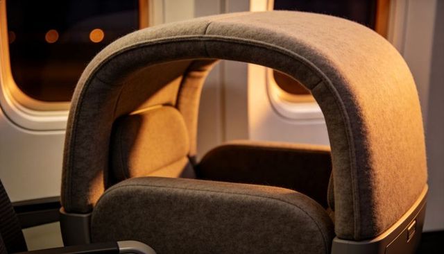 Luxury airplane privacy hood seat with curved shell and amber cabin lighting, first-class travel