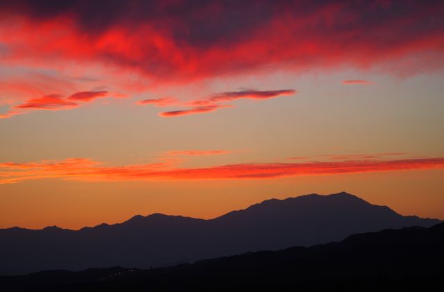 Vibrant sunset scene with red and orange hues illuminating sky above mountain range. Silhouette of peaks enhances tranquil mood, creating sense of calm. Ideal for travel brochures, nature photography, backgrounds, or inspirational content, emphasizing beauty of natural landscapes.
