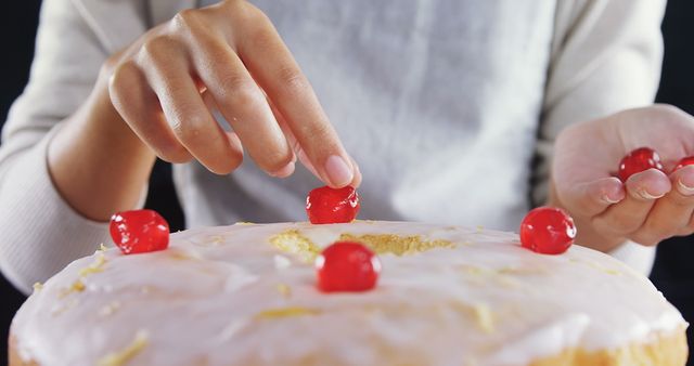 Mid section of woman topping a fresh baked cake with cherry 