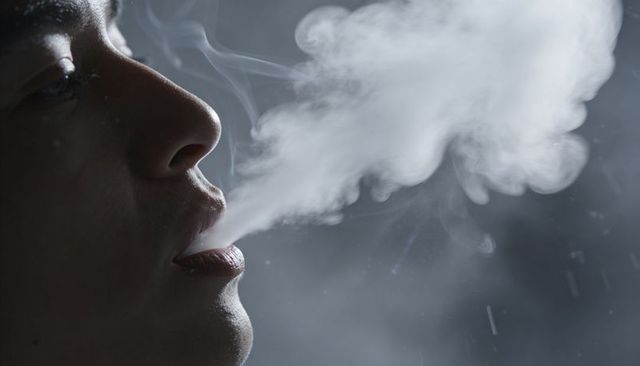 Male profile exhaling dense vapor plume in moody low-key portrait with rimlight