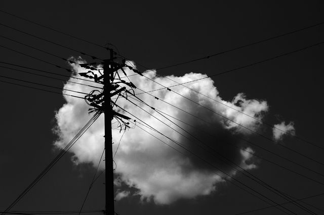 Silhouette of utility pole and wires against cloudy sky in black and white. Ideal for themes around urban infrastructure, electricity, technological connections, and artistic dramatic contrast. Suitable for use in backgrounds, presentations, and industrial-themed graphics.
