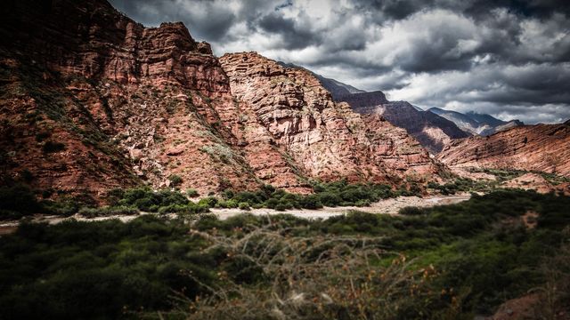 Dramatic mountain landscape featuring rocky cliffs and a stormy sky with dark clouds. Ideal for promoting outdoor adventures, travel destinations, nature conservation efforts, weather forecasts, or as compelling wall art for adding a dramatic touch to indoor settings.