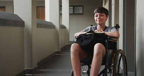 Confident Boy in Wheelchair Holds Notebook in Modern Corridor