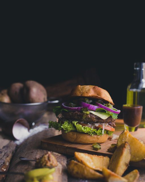 A beautifully presented gourmet beef burger with fresh lettuce, tomatoes, onions, and a brioche bun sits on a rustic wooden table next to a side of crispy potato wedges. This image is ideal for use in food blogs, restaurant menus, culinary websites, or for promoting new gourmet burger recipes.
