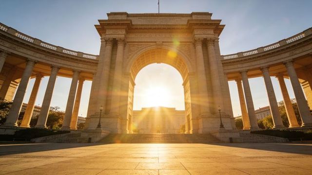 Golden sunrise backlighting neoclassical triumphal arch and sweeping colonnades at plaza