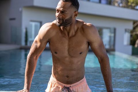 African american man emerging from luxury pool pushing up on edge in peach swim trunks