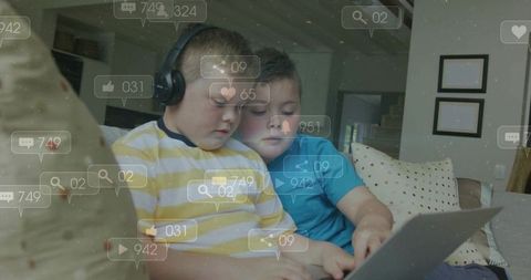 Brothers sharing laptop on couch wearing headphones browsing social media and learning