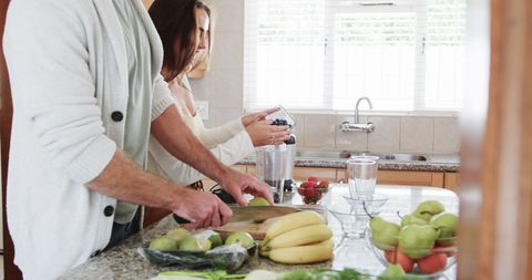 Joyful Couple Preparing Fruit Smoothie in Sunny Kitchen