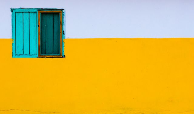 The photo showcases a colorful minimalistic window set on a vividly contrasting yellow and white wall. The turquoise blue window stands out against the bright background, making a bold visual statement. Ideal for use in design projects, architectural inspirations, art pieces, or modern themed decor. This image vividly captures the essence of simplicity and vibrancy, making it perfect for creative backgrounds, design elements, and advertisements focused on modern aesthetics.
