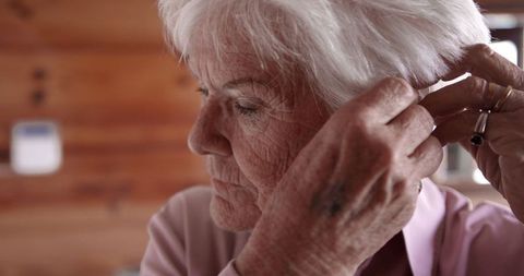 Senior Woman Adjusting Hearing Aid with Care at Home