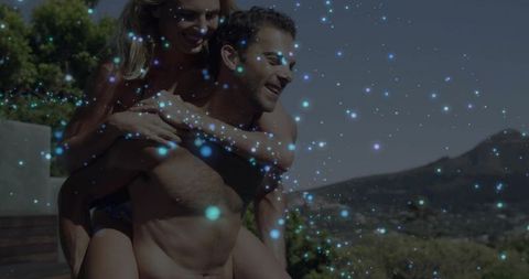 Couple on terrace piggybacking and laughing under sunshine with blue sparkle overlay