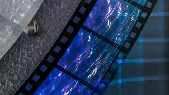 Iridescent 35mm film strip crossing reflective scanner grid closeup with prismatic sheen