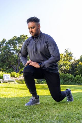 African american man performing forward lunge outdoor fitness training on sunlit lawn