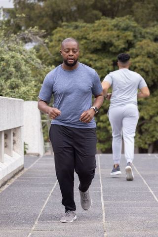African american men jogging on urban bridge wearing smartwatch tracking fitness progress