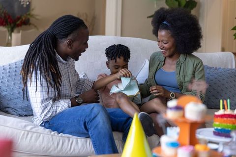 African american family celebrating child's birthday opening gift with rainbow cake