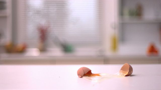 Depicts a raw egg cracking open on a kitchen counter in slow motion. The video highlights broken eggshells and the yolk spreading out messily. Ideal for use in culinary blogs, food safety articles, cooking tutorials, kitchen disaster articles, or food waste awareness campaigns.