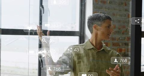 Mature female presenter showing social media metrics on glass wall in modern loft office
