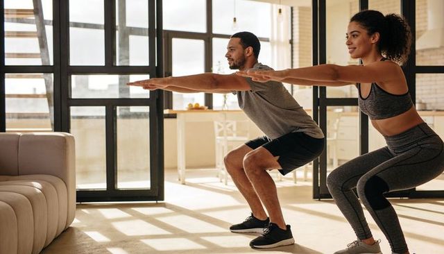Couple exercising together in bright modern apartment performing squats for home fitness