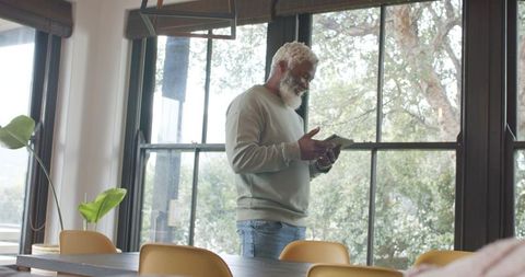 Senior Man Relaxing with Tablet by Sunny Dining Room Window