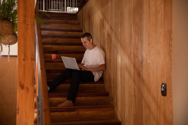 Man Working on Laptop While Sitting on Wooden Staircase at Home - Download Free Stock Photos Pikwizard.com