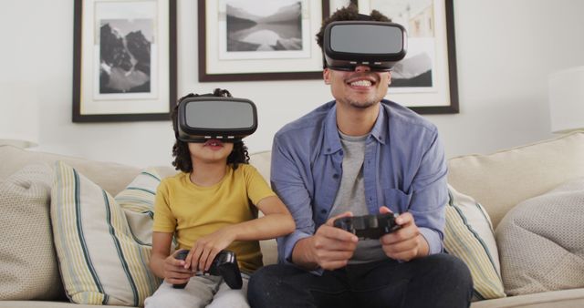 Father and son seated on a couch, engaged in virtual reality video gaming using VR headsets and game controllers. Artistic nature photographs on the wall create a cozy and immersive atmosphere. Ideal for themes of family bonding, modern technology, home entertainment, and leisure activities.