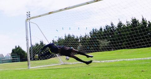 Goalkeeper diving to block soccer ball near goalpost