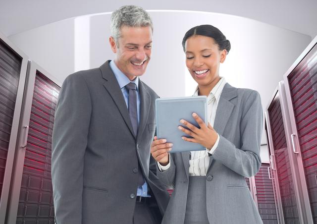 Business professionals smiling while discussing over a digital tablet, standing in a modern server room. Ideal for use in technology, business partnerships, data analysis, IT infrastructure, corporate communications, and high-tech industries.