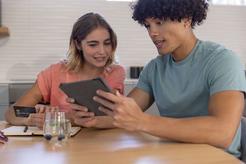 Young couple using tablet and credit card at kitchen table planning online payment