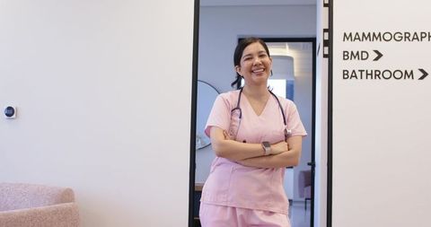 Smiling female nurse standing in clinic doorway wearing pink scrubs and stethoscope