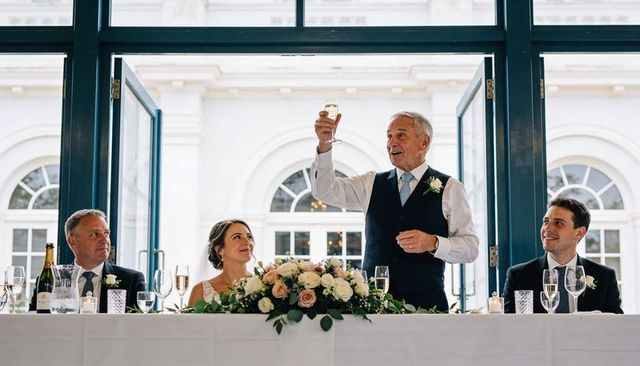 Father of bride raising champagne toast at wedding head table with rose centerpiece