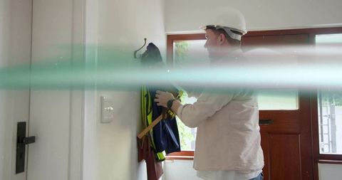 Construction worker wearing hard hat hanging high-visibility jacket in residential entryway