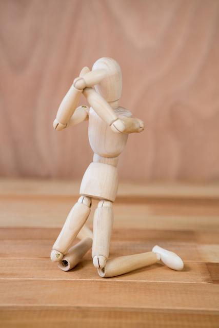 Wooden art mannequin posed to express emotion on a wooden floor. Useful for illustrating concepts of creativity, human emotion, and artistic expression. Ideal for art and design projects, educational materials, and creative workshops.