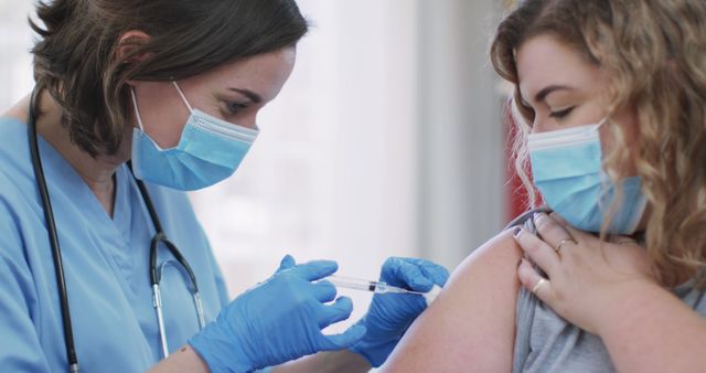 Medical professional gives vaccine injection to young woman who wears protective face mask. Ideal for promoting health-related articles, blogs, and campaigns focusing on vaccination, immunization, healthcare services, and pandemic safety protocols.