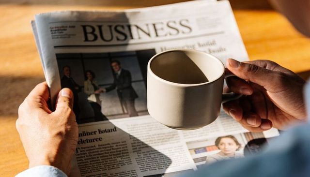 Morning business routine holding business newspaper and ceramic coffee mug in sunlight