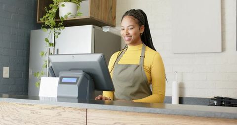 African american barista using touchscreen pos at modern minimalist cafe counter