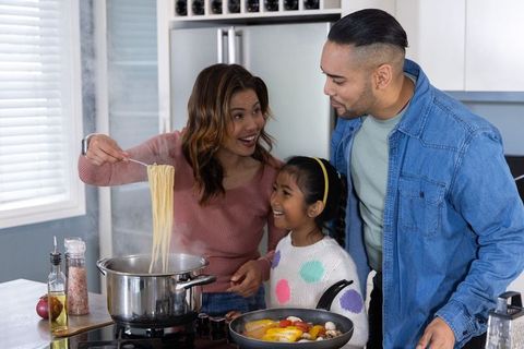 Family cooking together: mother lifting steaming pasta as child and father smiling