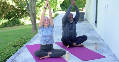 Senior diverse couple practicing outdoor yoga and meditating on purple mats on home patio