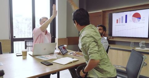 Coworkers celebrating success with high-five at meeting