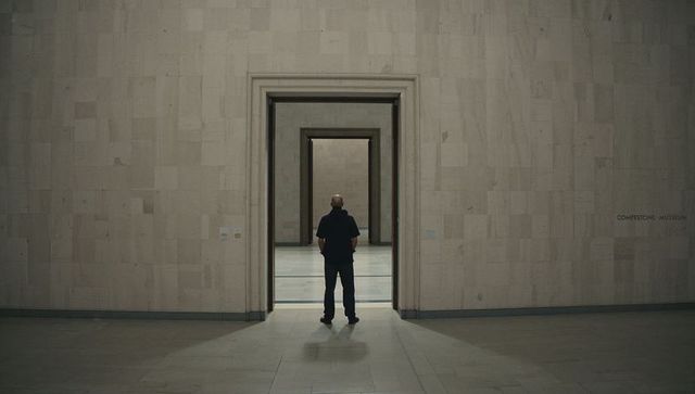 Solitary man standing in symmetrical minimalist museum galleries with receding doorways