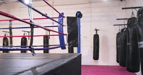 Boxing ring corner revealing hanging heavy bags and ropes in industrial training gym