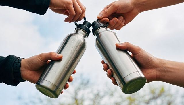 Friends clinking stainless steel water bottles outdoors celebrating hydration and sustainability