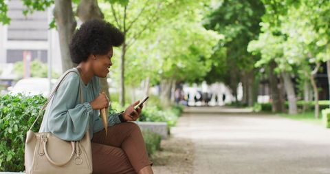 Smiling Businesswoman Using Smartphone in Green City Park