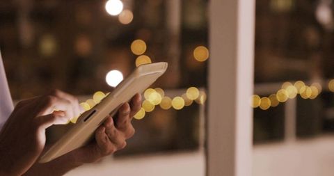 Tapping Tablet at Night with Warm Bokeh Lights Urban Evening Tech Lifestyle and Intimacy