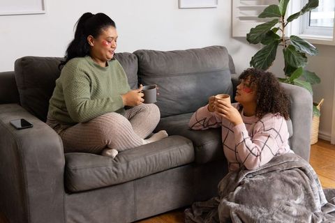 Friends relaxing, chatting on couch with eye patches and coffee mugs in cozy living room