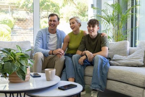 Smiling family sharing laughter on modern sectional sofa in bright living room with plants